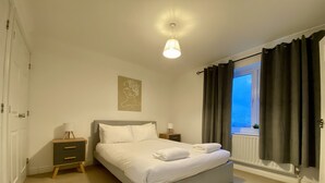 A neatly arranged bedroom with a bed, bedside tables, a wall art piece, and a window with curtains.