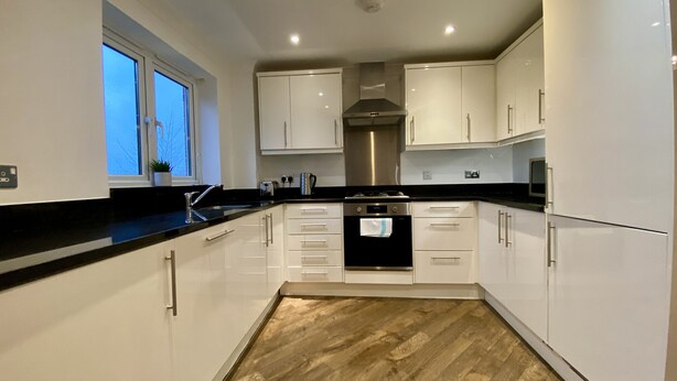 A modern kitchen with white cabinets, a black countertop, and a stainless steel oven.