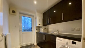 A compact kitchen with dark cabinets, a built-in washing machine, and a window with a view of bare trees.