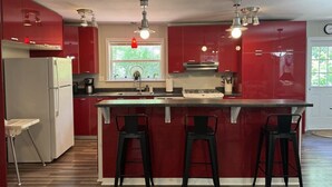 Een moderne keuken met rode kastjes, een witte koelkast en een centraal kookeiland met barkrukken.