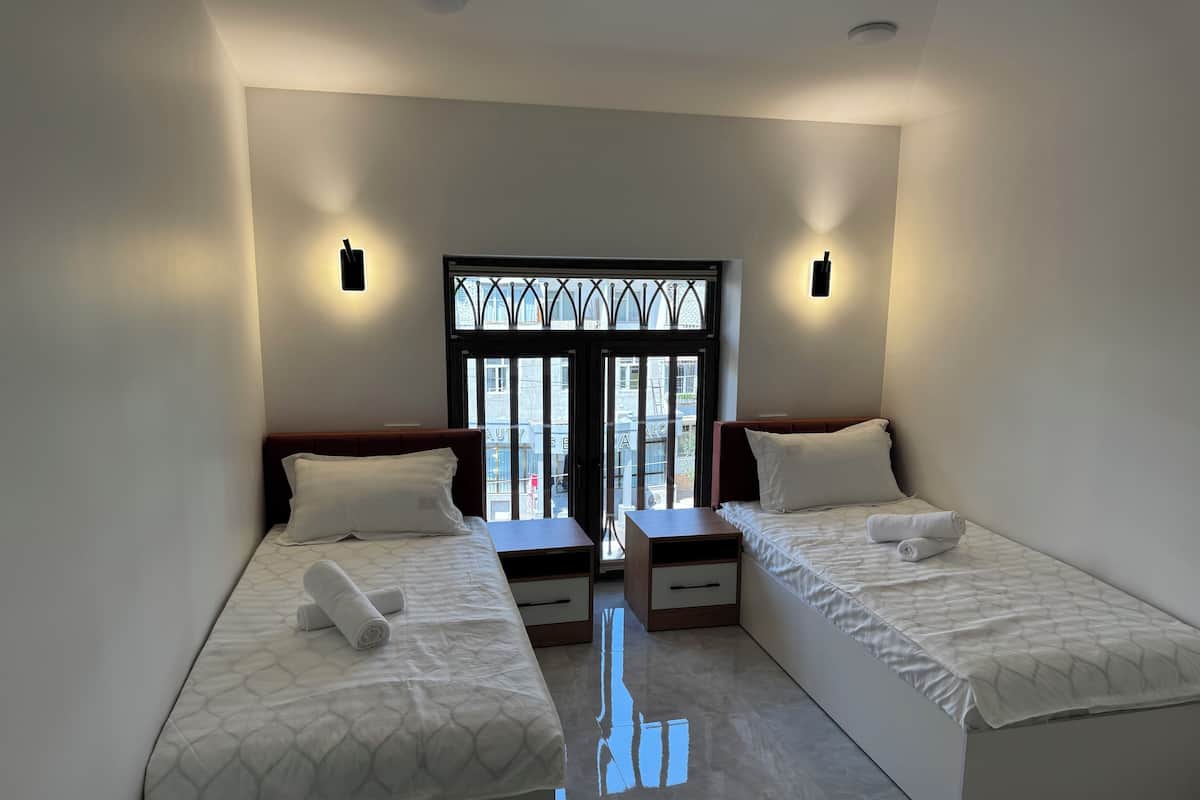 A hotel room with two single beds, a small table, and a window with a view of the street.