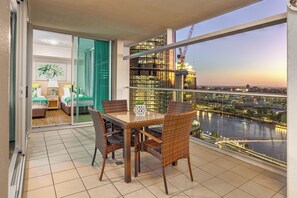 A balcony with a dining table and chairs, a sliding glass door leading to a bedroom, and a view of a cityscape and river at dusk. - Oasis Retreat Level 27 in Casino Towers (Brisbane)
