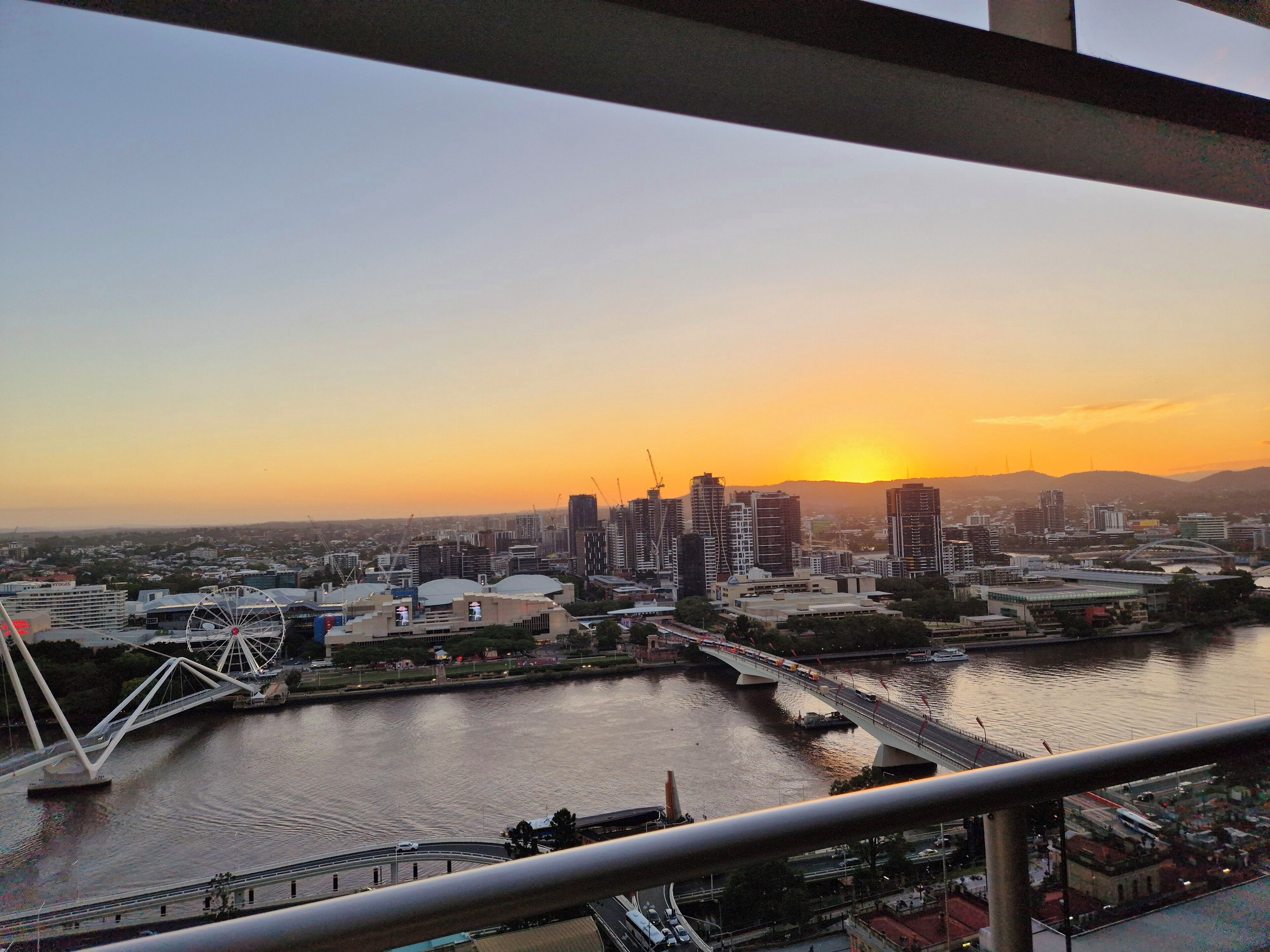 A cityscape with a river, bridges, and high-rise buildings during sunset.