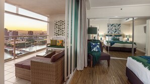 A spacious hotel room with a balcony overlooking a cityscape and river.
