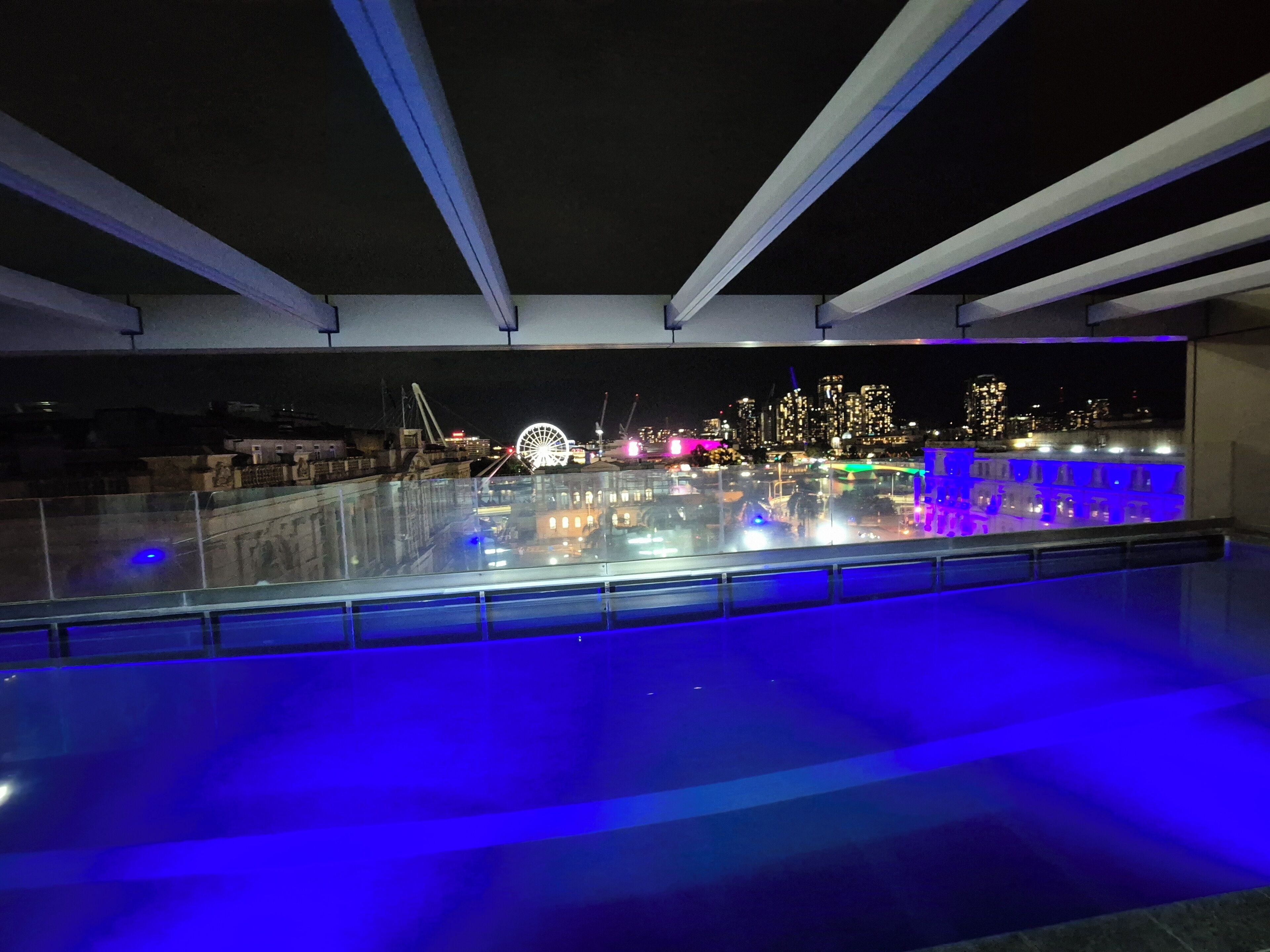 A rooftop pool with a cityscape view, including a Ferris wheel and illuminated buildings.