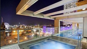 A modern rooftop pool area with a view of a cityscape at night, including a Ferris wheel.