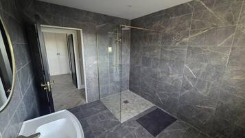 A modern bathroom with a glass-enclosed shower, a white sink, and dark marble walls.