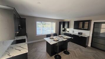 A modern kitchen with dark cabinetry, a marble countertop, and a herringbone wood floor.