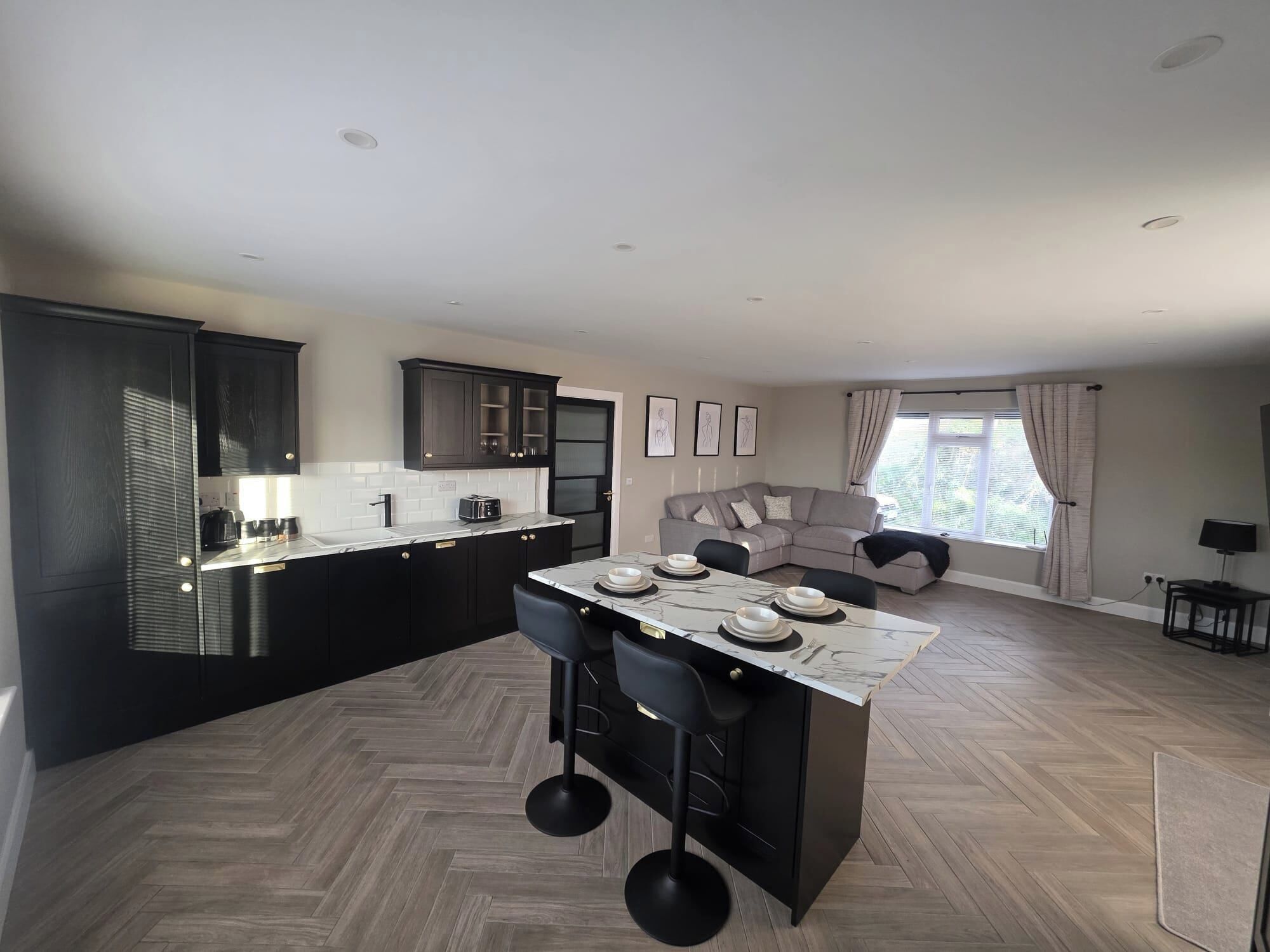 A modern kitchen with dark cabinetry, a marble countertop, and a central island with bar stools.