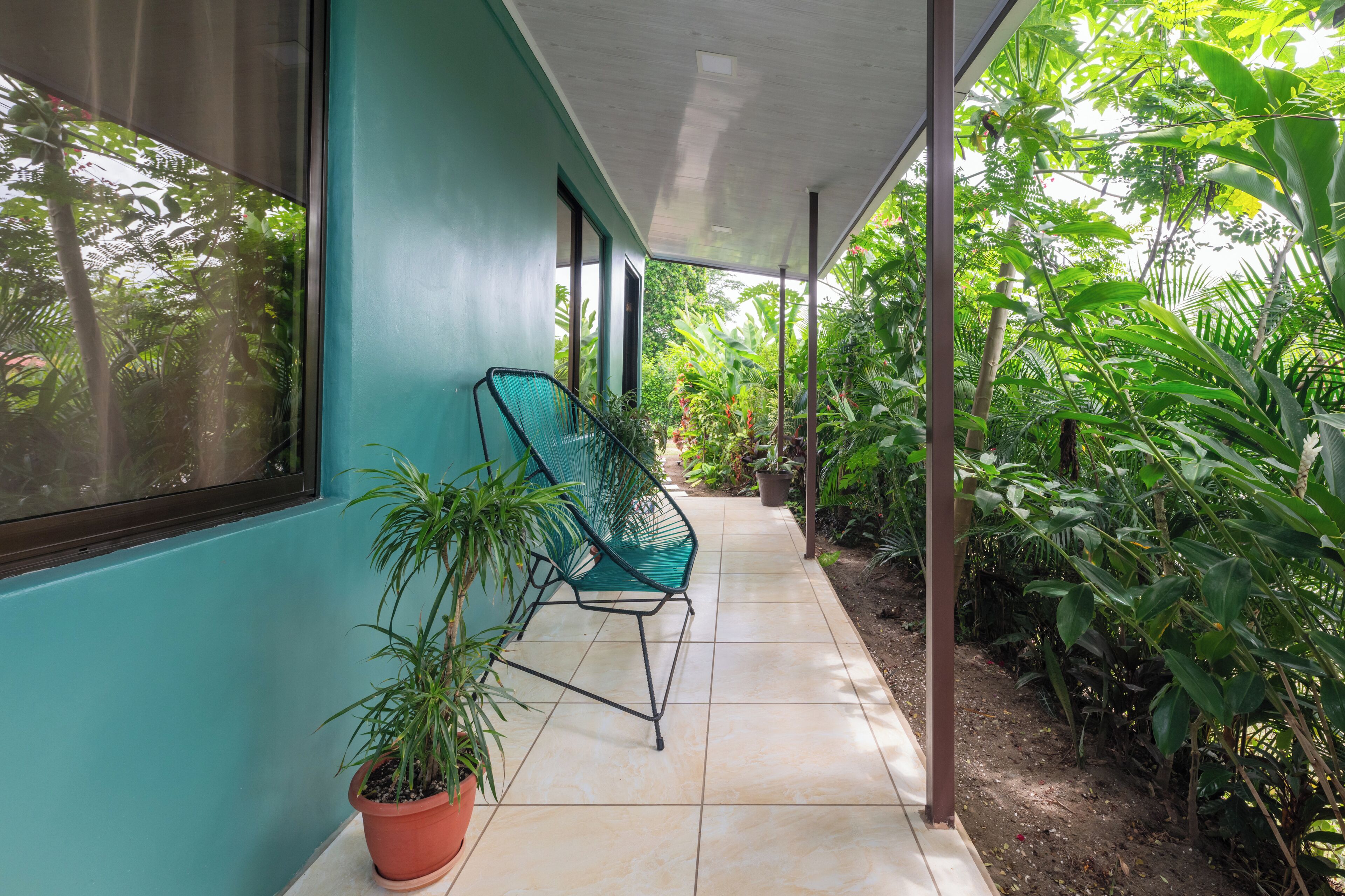 A covered outdoor area with a tiled floor, a green chair, and potted plants.