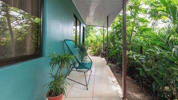 A covered outdoor area with a tiled floor, a green chair, and potted plants.