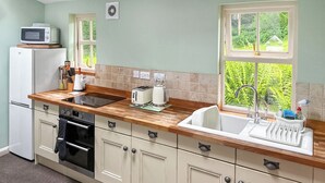 Une cuisine équipée d’un évier, d’une cuisinière, d’un four à micro-ondes et d’une fenêtre donnant sur un espace verdoyant.