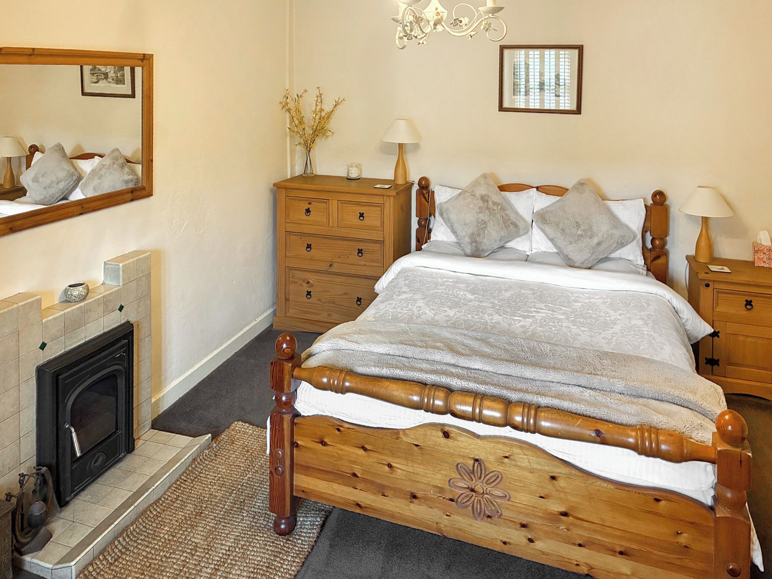 A bedroom with a wooden bed, a dresser, a mirror, a fireplace, and a chandelier.