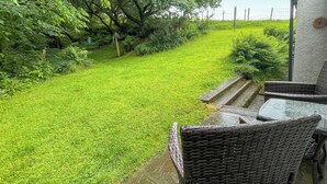 Une cour arrière verdoyante avec une terrasse en bois et des meubles en osier.