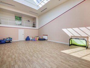A spacious room with a high ceiling, a balcony, a children's play area, and a sports goal.