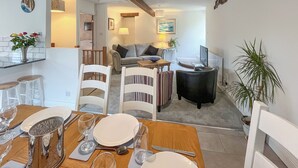 A dining area with a wooden table set for four, a sofa, and a TV in the background.
