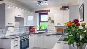 A modern kitchen with white cabinets, a black countertop, and a stainless steel sink. There is a window with a view of greenery outside, and a vase with flowers on the countertop.