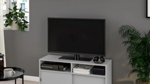 A modern living room with a grey wall, a flat-screen TV on a white entertainment unit, a coffee table with a white mug, and two potted plants. - Studio Sleeps3- CloseTo OldTrafford - WhP- o2 (Manchester)
