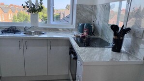 A modern kitchen with white cabinets, a built-in oven, a sink, and a window with a view of houses. - Studio Sleeps3- CloseTo OldTrafford - WhP- o2 (Manchester)