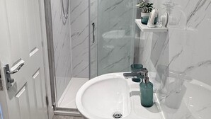 A modern bathroom with a glass shower enclosure, a white sink with a green soap dispenser, and a small shelf with toiletries. - Studio Sleeps3- CloseTo OldTrafford - WhP- o2 (Manchester)