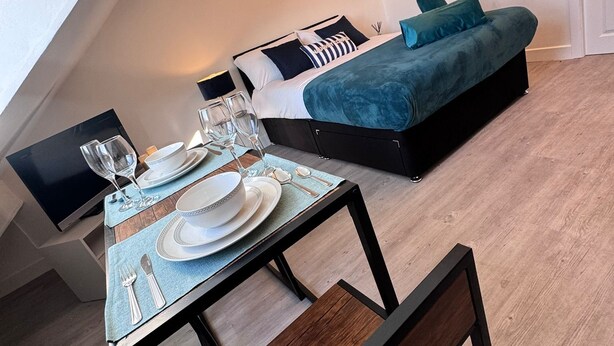 A modern bedroom with a bed, a sofa, and a dining area set up with plates, glasses, and cutlery. - Studio Sleeps3- CloseTo OldTrafford - WhP- o2 (Manchester)