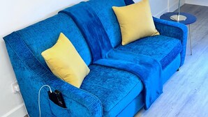 A blue sofa with yellow cushions in a room with a blue floor lamp. - Studio Sleeps3- CloseTo OldTrafford - WhP- o2 (Manchester)