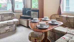 Un salon chaleureux avec une table à manger en bois, mise pour quatre personnes, entourée de canapés à motifs et d’un téléviseur.