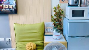 Une pièce confortable avec un fauteuil à coussins verts, une petite table avec une horloge, un ventilateur et un four à micro-ondes.