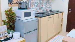 Une cuisine compacte équipée d’un four à micro-ondes, d’une bouilloire et d’un réfrigérateur. On y trouve une petite table avec un calendrier et une paire de chaussons.