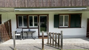 A building with a covered patio area, a table and chairs, and a wooden fence.