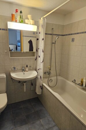 A bathroom with a sink, toilet, and bathtub. There is a shower curtain with a floral pattern. - Bergecho EG Mitte by Interhome (Lenk)
