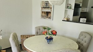 A round dining table with four upholstered chairs, a vase with flowers, and a hanging light fixture.