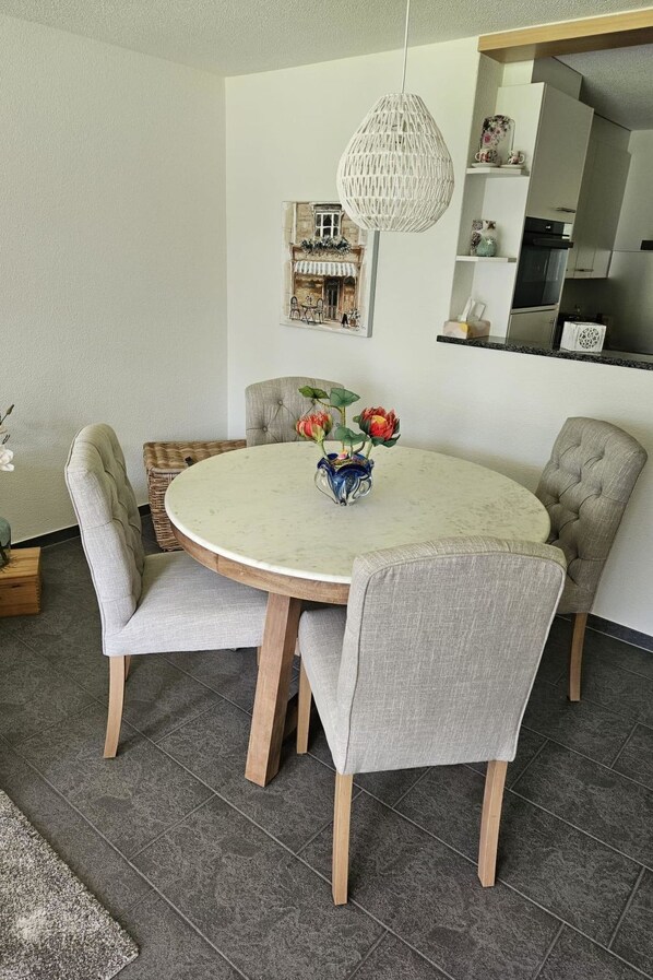 A round dining table with four upholstered chairs, a vase with flowers, and a hanging light fixture. - Bergecho EG Mitte by Interhome (Lenk)