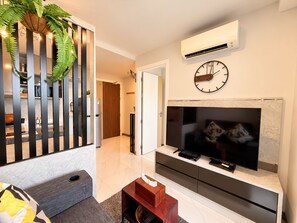 A modern living room with a flat-screen TV, a clock, and an air conditioning unit on the wall. - A303 - 1 Bedroom Serviced Apartment Partial Sea View at Ao Nang Beach (Tambon Ao Nang)