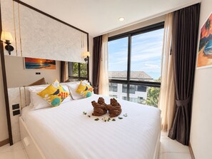 Ein Hotelzimmer mit einem großen Bett, zwei Kissen mit Blumenmuster, einer Teddybären-Anordnung und einem Gemälde eines Sonnenuntergangs.