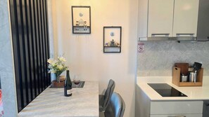 A compact kitchen with a marble countertop, a sink, and a cabinet. There is a dining table with a vase of flowers and a wine bottle.