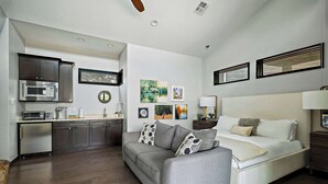 A compact living space with a kitchenette, a sofa, a bedside table, and artwork on the walls.