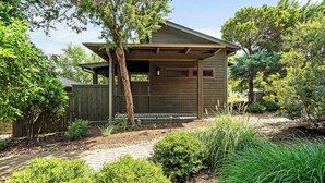 A wooden house with a covered porch, surrounded by trees and a garden.