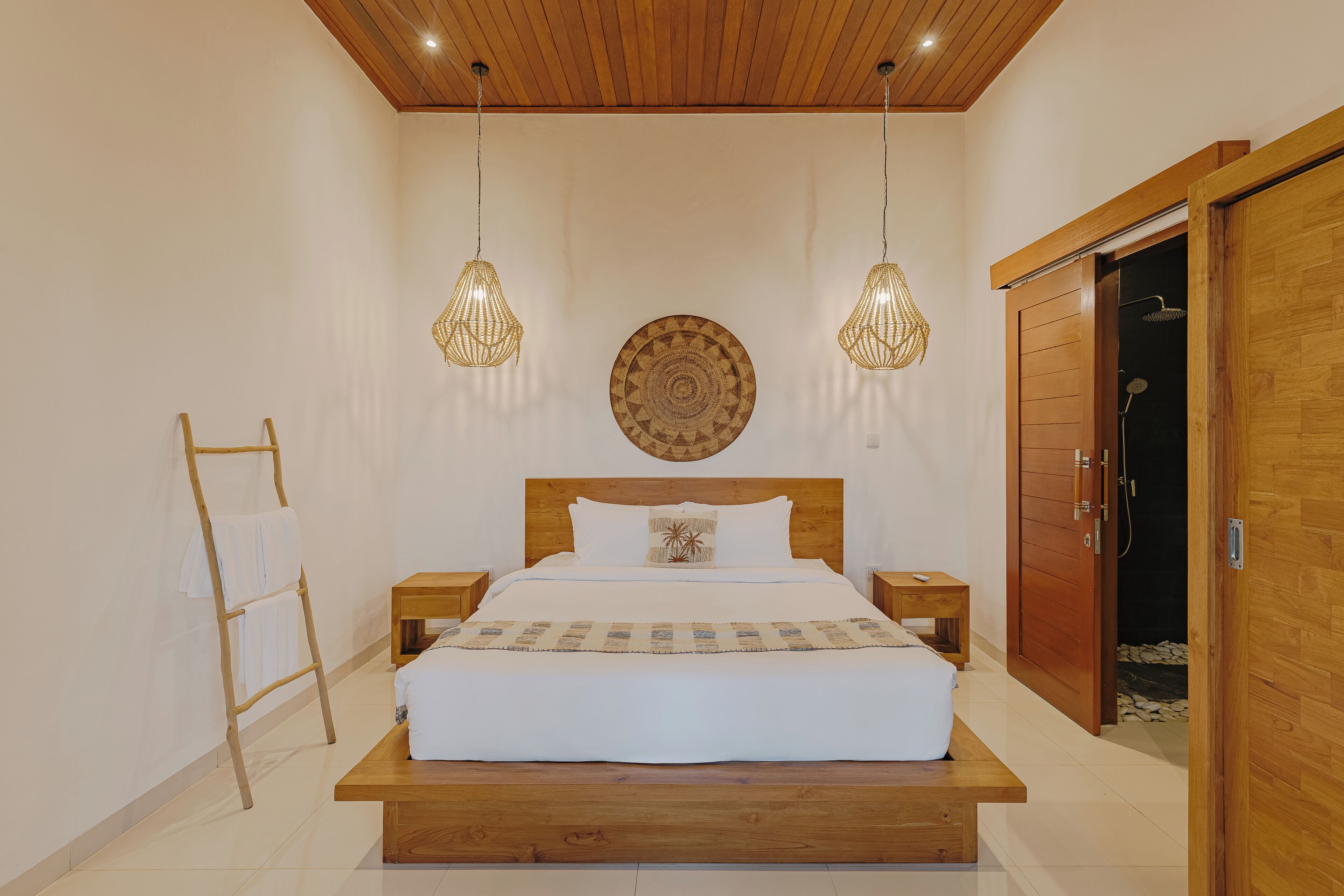 A bedroom with a wooden bed, two bedside tables, a ladder with towels, a wooden wardrobe, and a circular wall decoration.