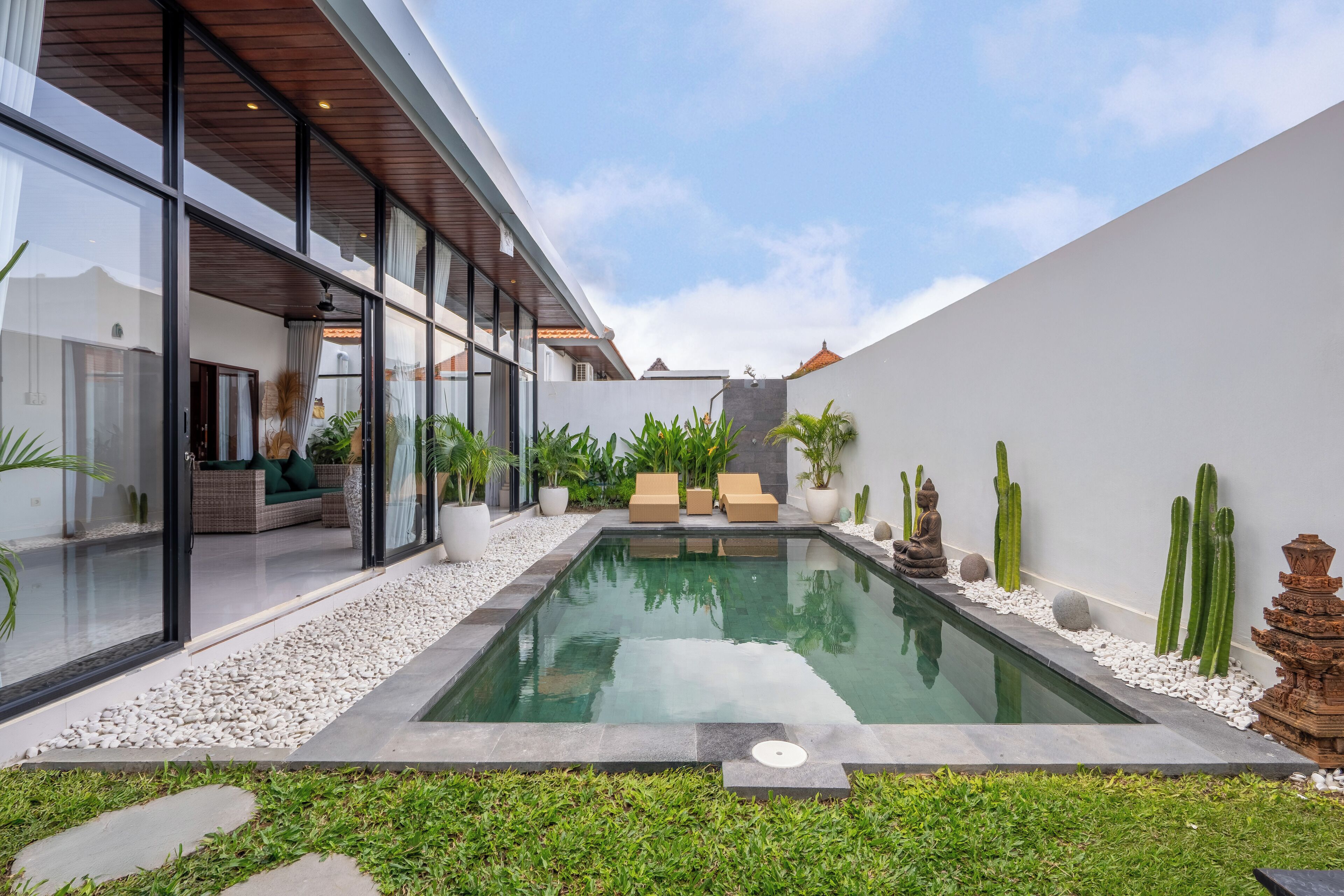 Et moderne poolområde udendørs med en lounge med glasfacade, hvide sten og kaktusser.