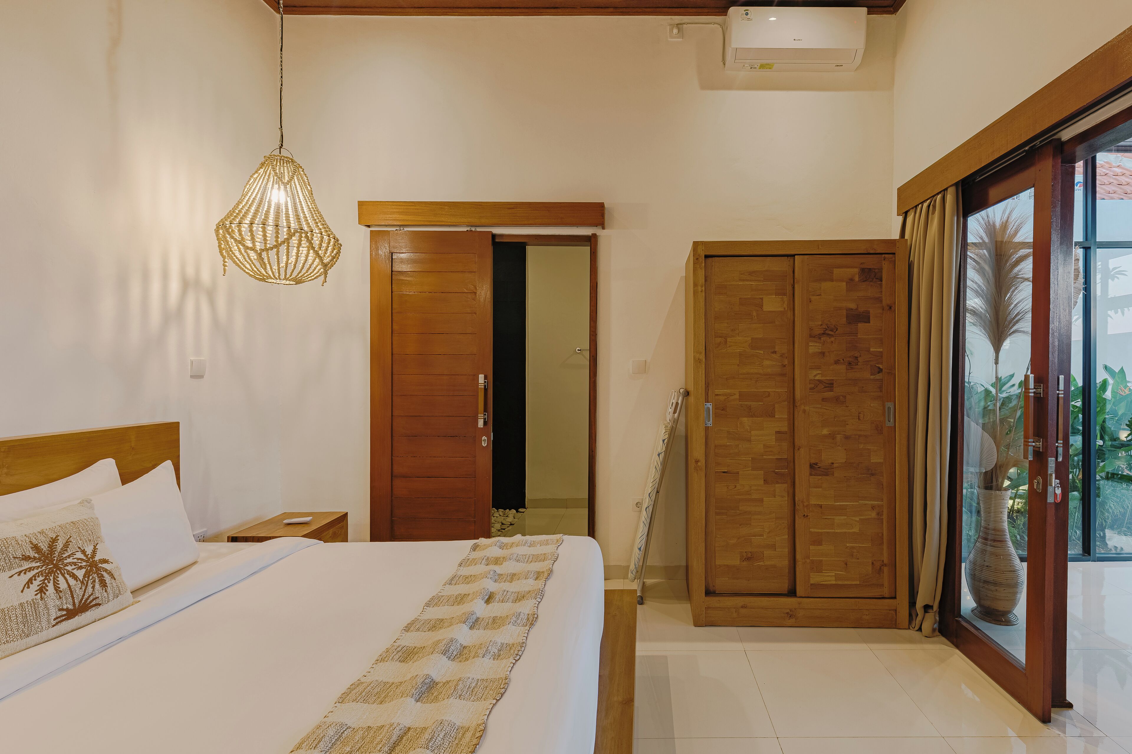 Een hotelkamer met een bed, een hanglamp, een houten garderobe en een schuifdeur naar buiten.