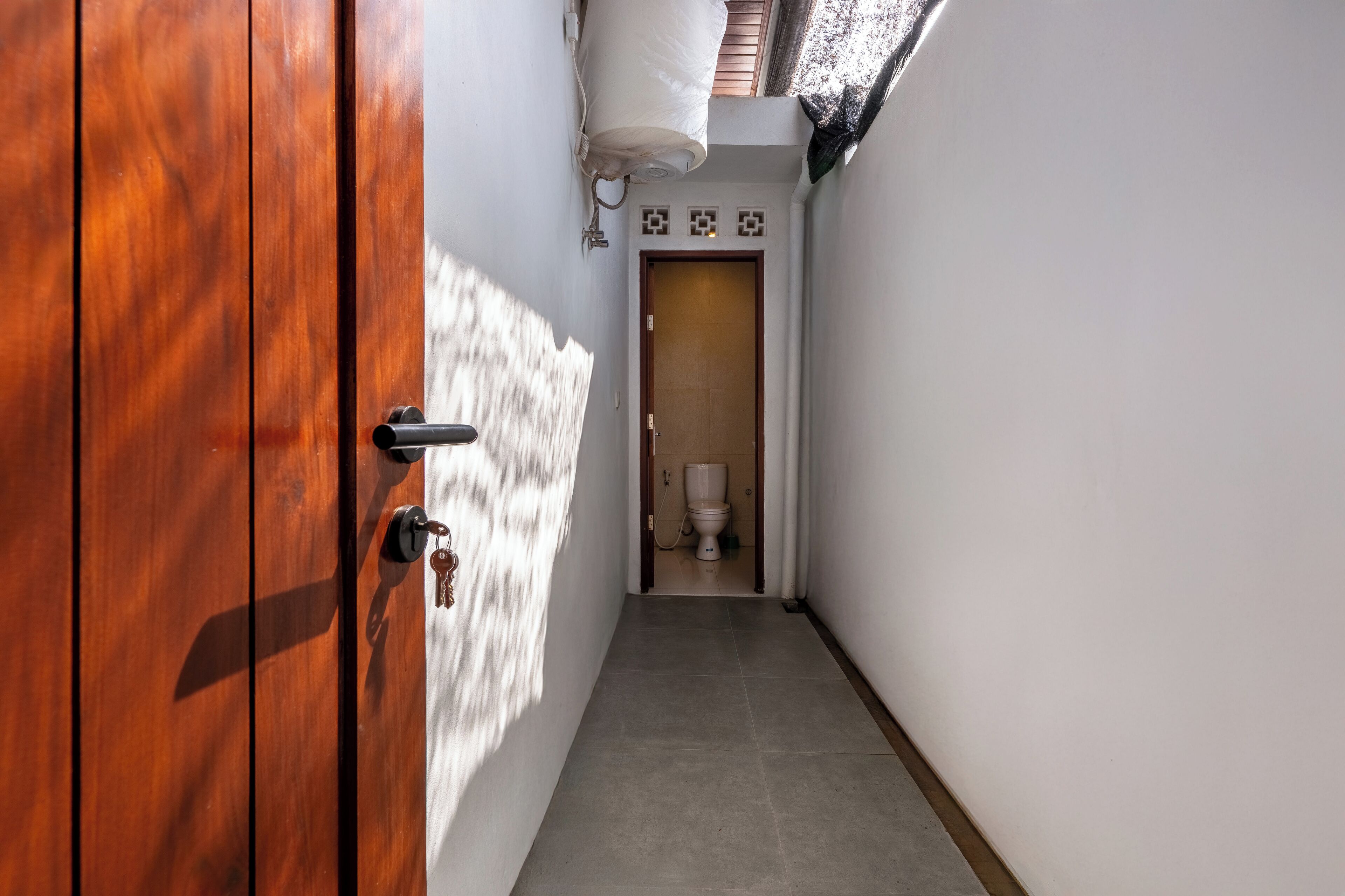 A narrow hallway with a wooden door on the left and a toilet visible in the distance.