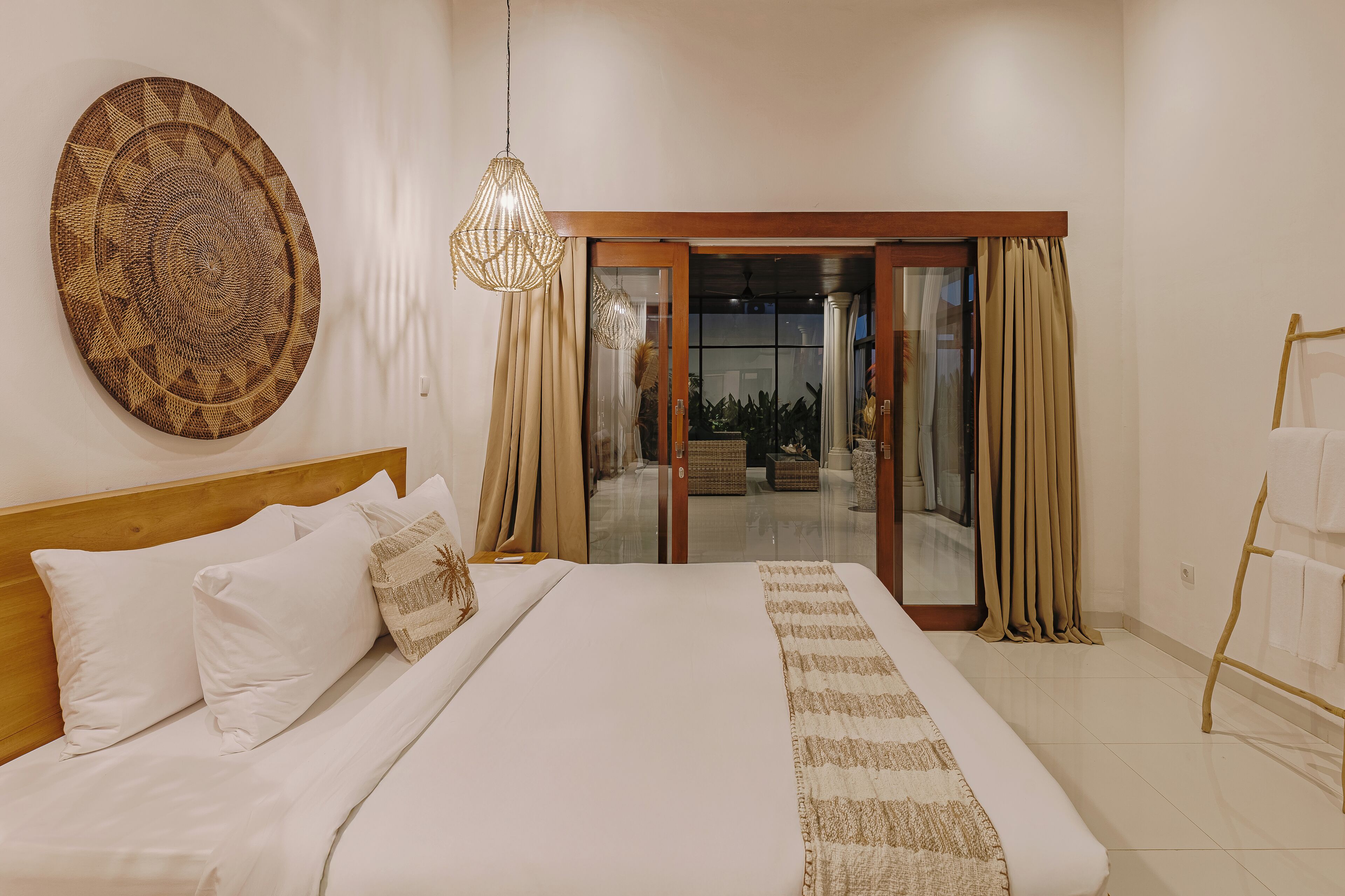 A bedroom with a large bed, a decorative wall hanging, and a view of the outdoor area through a glass door.