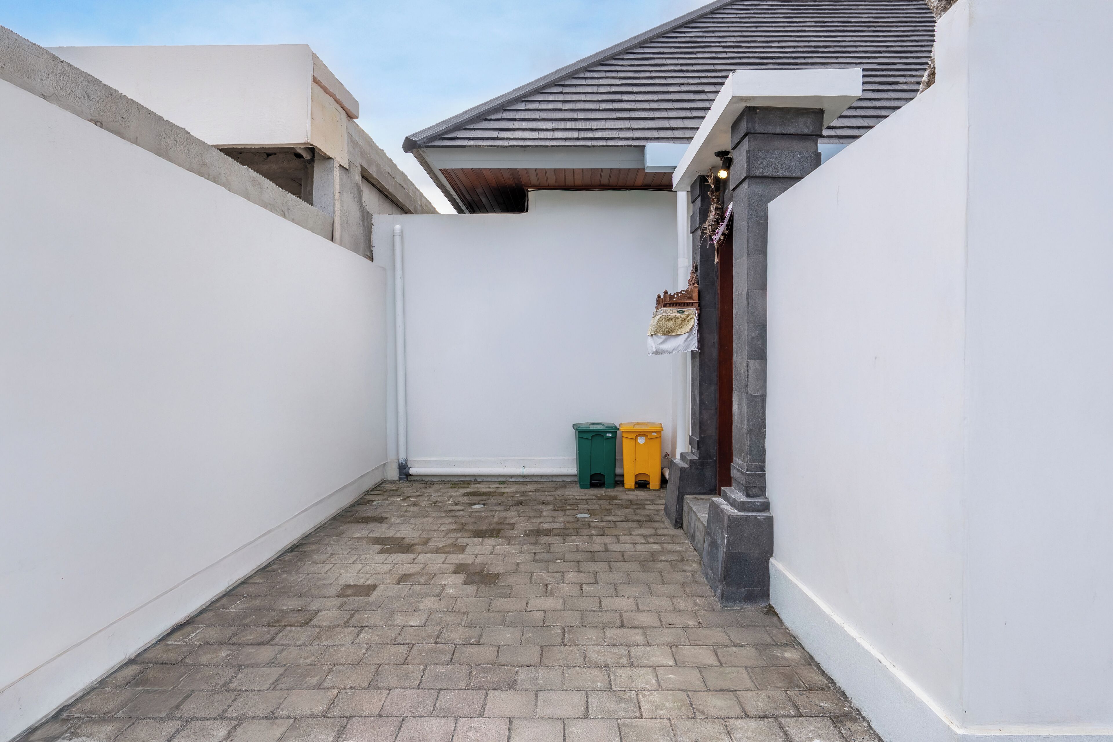 A narrow alleyway with a tiled floor, white walls, and a small trash bin.