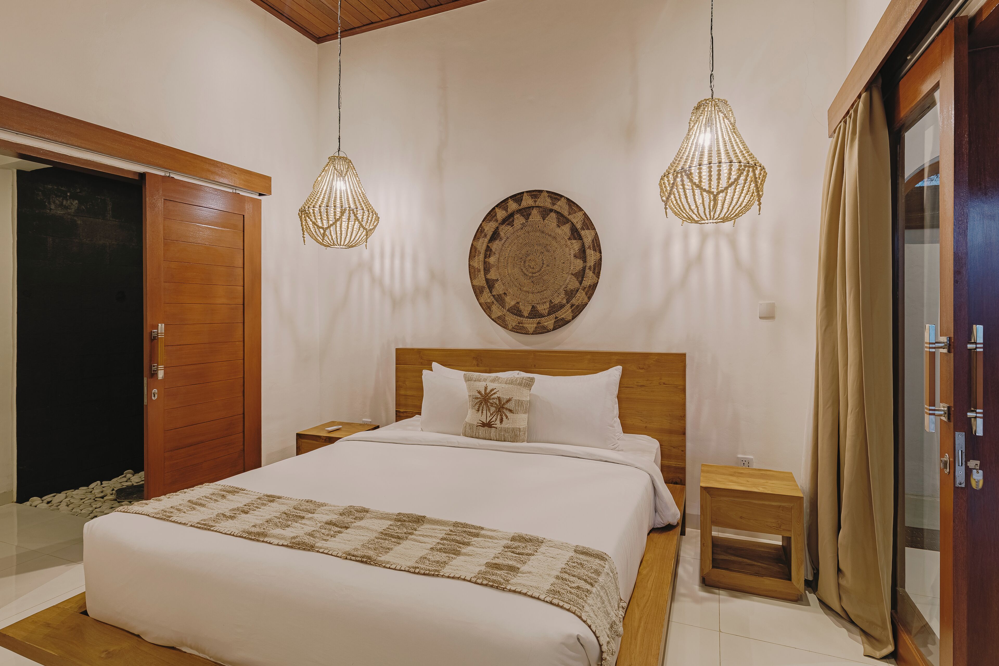 Ein Schlafzimmer mit einem hölzernen Bett, zwei Nachttischen, einem Holzschrank, einem gewebten Wandbehang und einer Pendelleuchte.
