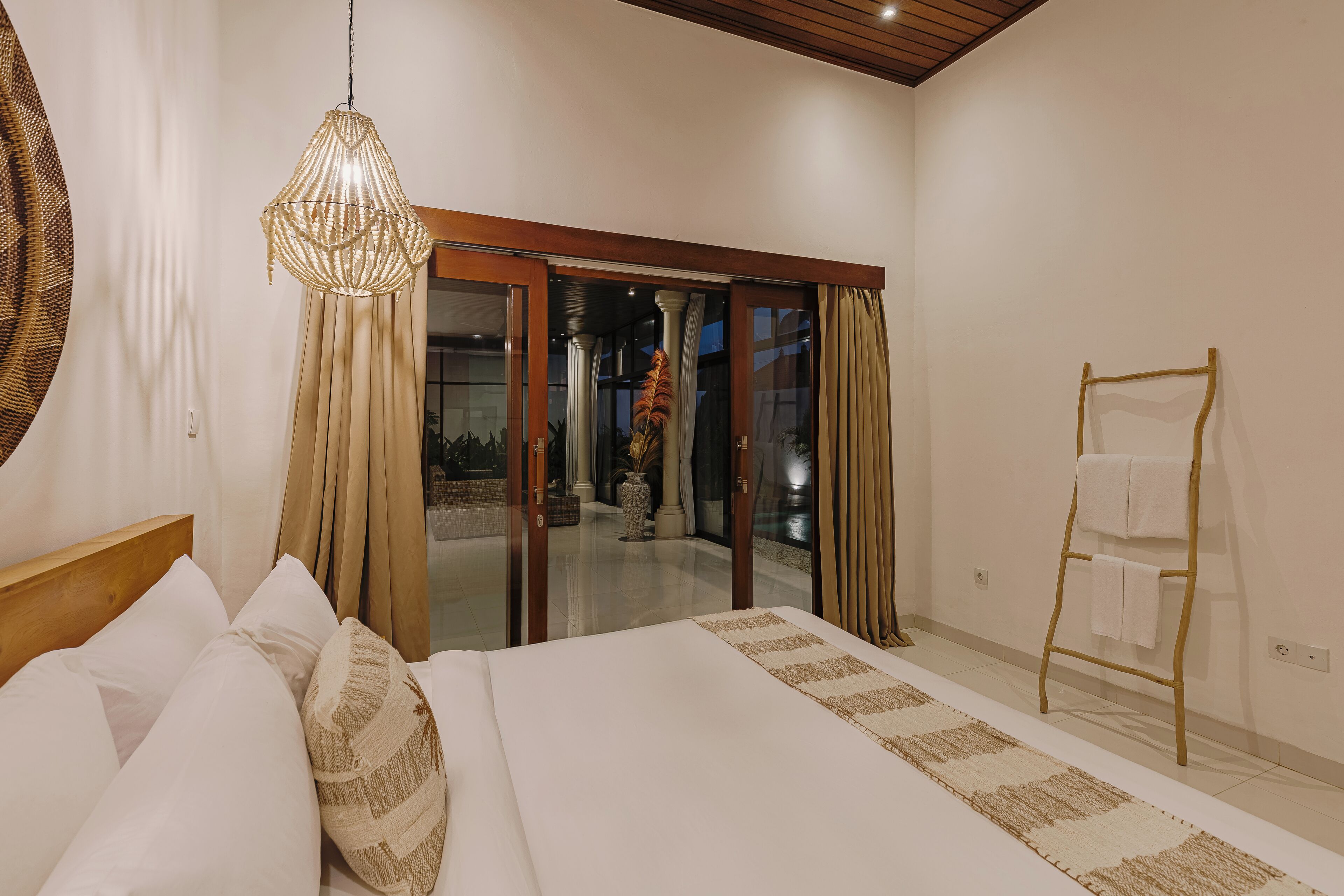 Un dormitorio con una cama, una lámpara colgante, una escalera de madera y vistas a través de un ventanal.