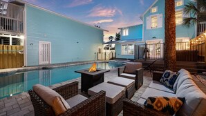 A poolside area with a fire pit, wicker furniture, and a staircase leading to a second-story balcony.