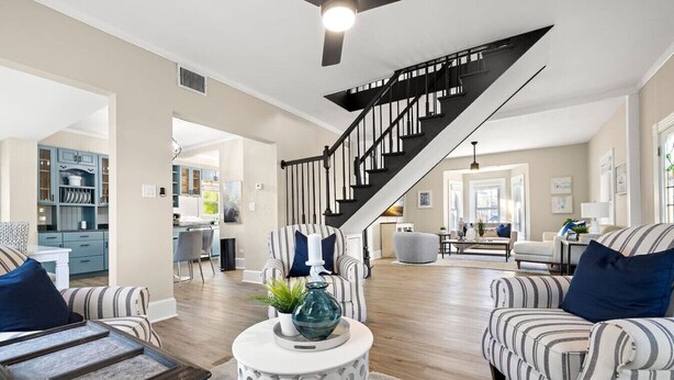 A spacious living room with striped sofas, a round coffee table, and a staircase leading to another level.