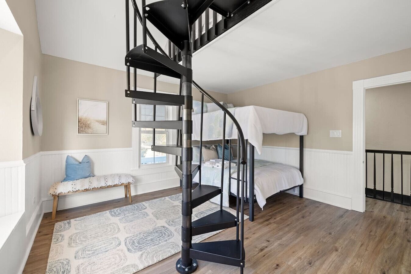 A compact bedroom with a black spiral staircase, a bunk bed, a bench, and a patterned rug.