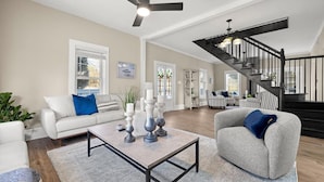 A spacious living room with a high ceiling, a staircase, and a large window.